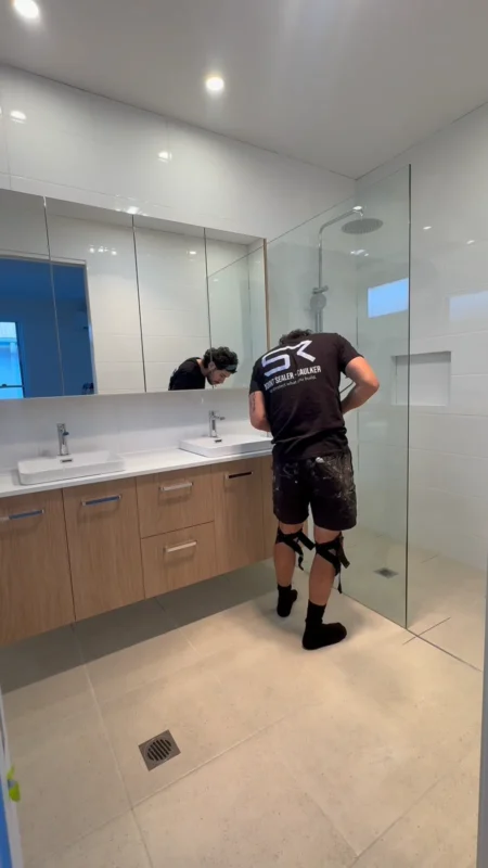 Technician preparing a frameless shower screen before applying silicone